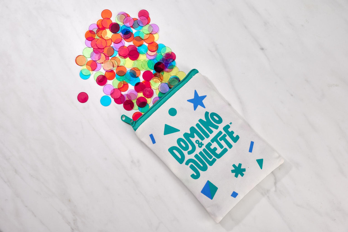 Colorful counting chips spilling from a Domino & Juliette bag on a white marble surface, kids early math education, sensory play.