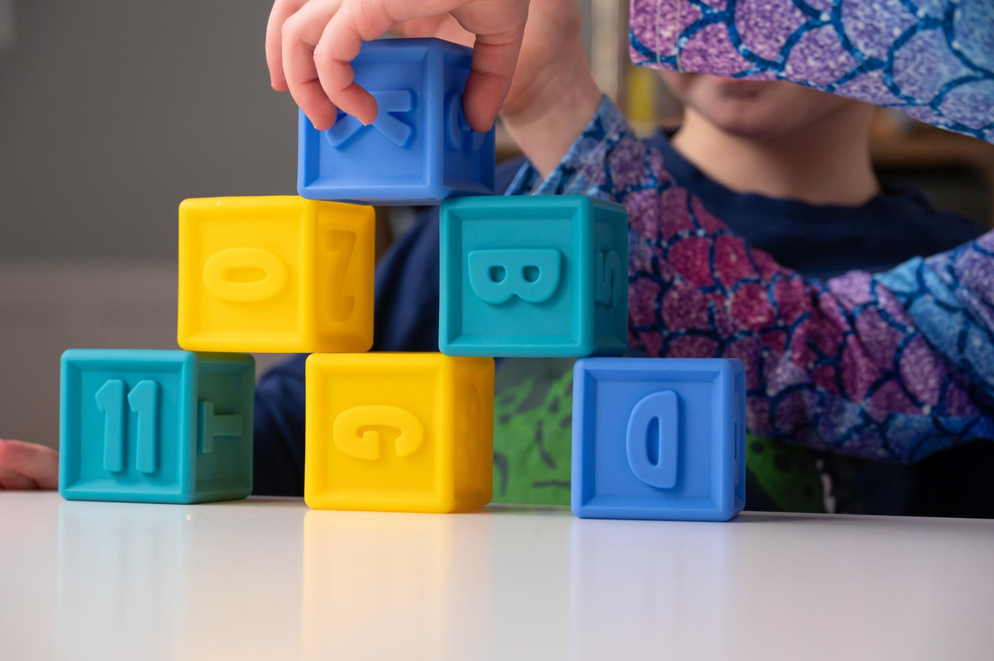 Child stacking colorful SQUEEZE & STACK alphabet blocks. Educational baby toy for learning letters and numbers.