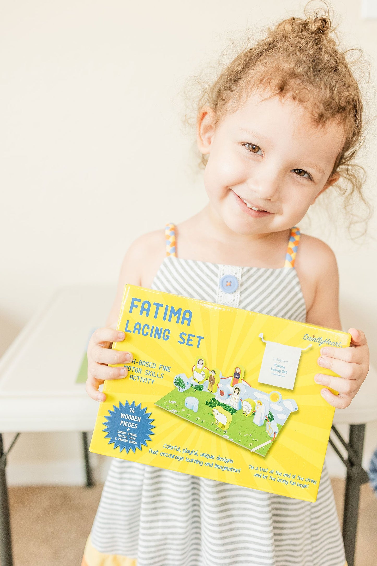 Toddler holds Saintly Heart Fatima Lacing Set. Wooden toy promotes fine motor skills. Puzzle Planet.