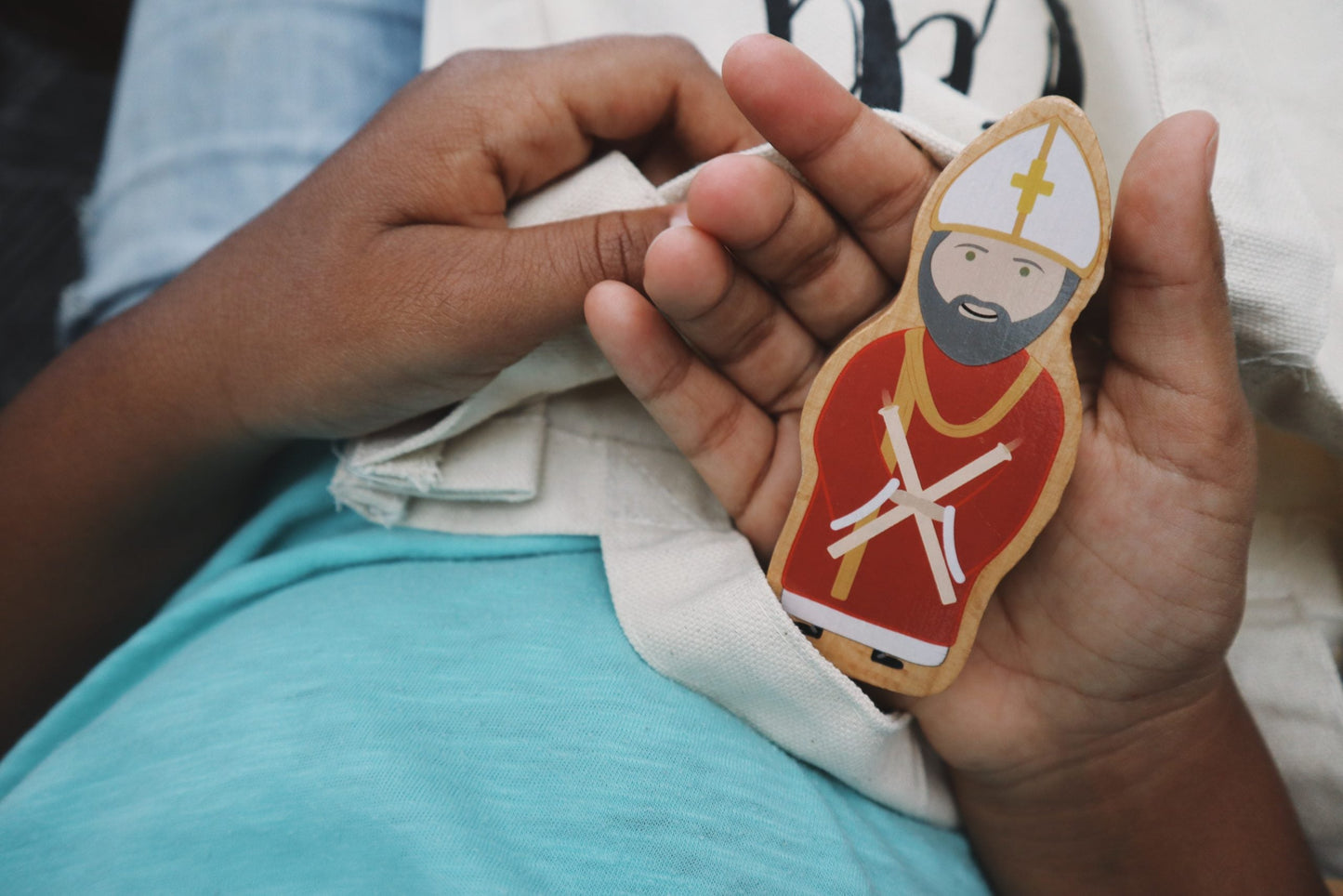 Child's hands holding a Saint Blaise wooden toy from Puzzle Planet. Catholic World Charity Set.