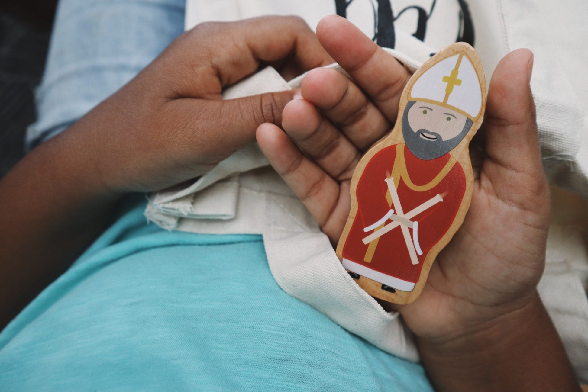 Child's hands holding a Saint Blaise wooden toy from Puzzle Planet. Catholic World Charity Set.