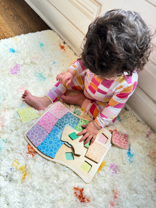 Baby playing with a colorful wooden prayer rug spatial reasoning puzzle on a soft rug. Child development toy.